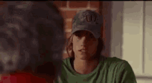 a man wearing a baseball cap and a green shirt is talking to another man in front of a brick wall .