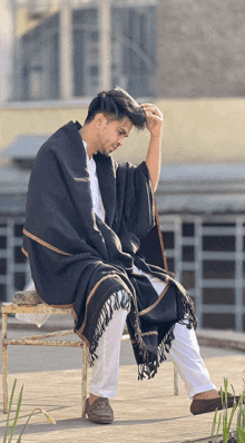 a man wearing a black poncho sits on a bench