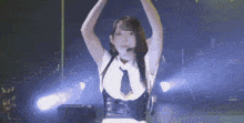 a woman in a white shirt and black tie is dancing on a stage with her arms in the air