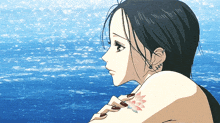 a girl with a tattoo of a flower on her arm looks out over the ocean