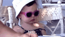 a baby wearing sunglasses and a hat is sitting on a chair .