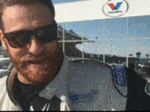 a man wearing sunglasses stands in front of a valveline sign