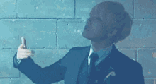 a man in a suit and tie is giving a thumbs up in front of a brick wall .