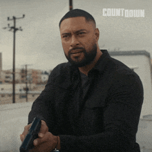 a man in a black shirt holds a gun in front of a countdown sign