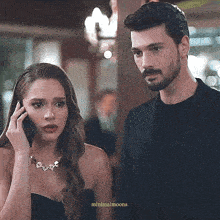 a man and woman are standing next to each other and the woman is talking on her phone