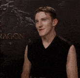a man in a black sleeveless shirt is smiling in front of a dragon poster