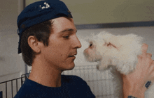 a man wearing a blue hat that says recycle on it holds a small white dog