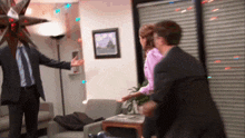 a man in a suit and tie is talking to a woman in a pink shirt in a living room