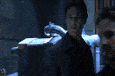 a man in a suit stands in a dark room with a blue light behind him