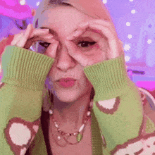 a woman in a green sweater is making a funny face while covering her eyes with her hands .