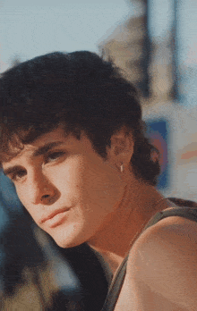 a young man wearing a tank top and earrings looks at the camera with a serious look on his face