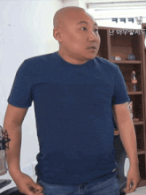 a bald man wearing a blue shirt stands in front of a shelf with a coca cola bottle on it