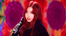 a woman with red hair and blue eyes is standing in front of a purple and red background .