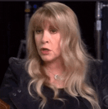 a close up of a woman 's face with long blonde hair and a necklace .