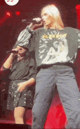 a woman is singing into a microphone on a stage while a man stands behind her .