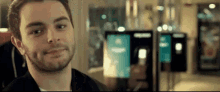 a man with a beard is smiling and looking at the camera in front of a row of vending machines .