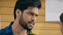 a man with a beard says i like it in front of a yellow wall .