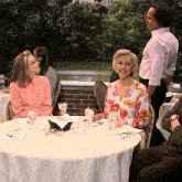 a woman in a pink shirt sits at a table with a white table cloth