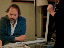 a man with a beard sits at a table with a newspaper and a computer monitor