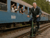 a man is riding a bike on the tracks in front of a train that says mav on it