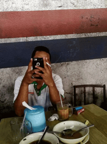 a man sitting at a table smoking a cigarette and taking a picture of himself with his phone