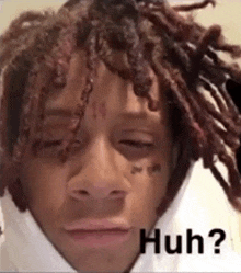a man with dreadlocks and a tattoo on his face is making a funny face with his eyes closed .