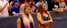 a couple of women standing next to each other in front of a crowd of people .