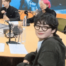 a group of people are sitting at a table with microphones . one of the people has pink hair .