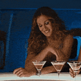 a woman sitting at a table with three martini glasses