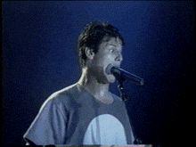 a man singing into a microphone with a blue shirt on