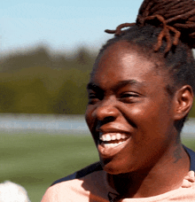 a woman with dreadlocks and a tattoo on her arm smiles for the camera