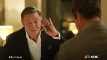 a man in a suit is talking to another man with #suitsla written on the bottom right