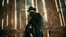 a woman wearing a cowboy hat and a black coat stands in front of a wooden fence