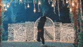 a man is holding a woman in his arms while standing in front of a fence with lights hanging from it .