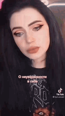 a woman with long black hair and blue eyes is wearing a black t-shirt and talking to the camera .