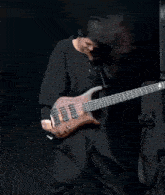 a man in a black shirt is playing a brown bass guitar