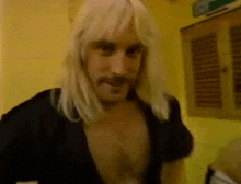 a man with long blonde hair and a mustache is standing in a room without a shirt on .
