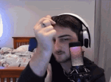 a man wearing headphones and a ring is standing in front of a microphone in a bedroom .