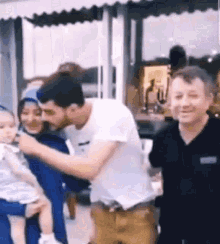 a man is holding a baby in his arms while standing next to a woman and a man .