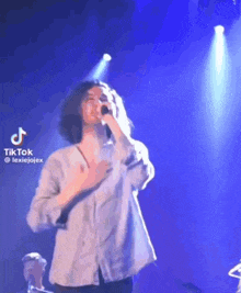a woman is singing into a microphone on a stage in front of a blue light .