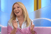 a woman in a pink shirt is sitting on a pink couch and laughing