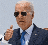 a man wearing sunglasses and a suit gives a thumbs up
