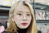 a woman wearing glasses and a black turtleneck is standing in front of a display of dolls .