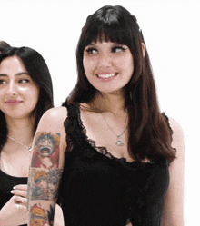 a woman with a tattoo on her arm is smiling and standing next to another woman .