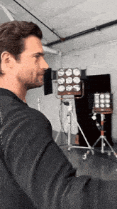 a man in a suit is standing in a room with a lot of lights on a tripod .