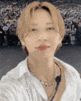 a man wearing a white shirt and a necklace with a microphone around his neck looks at the camera