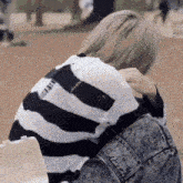 a person wearing a black and white striped sweater and a denim jacket is sitting down .