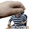 a man in a striped shirt is sitting at a table while a hand reaches out towards him .