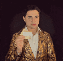 a man in a gold jacket is holding a piece of paper with the letters s on it