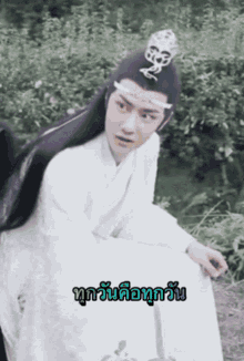 a man in a white robe with a crown on his head is sitting in a field